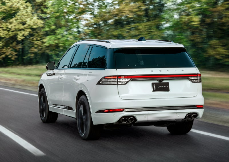 A white 2026 Lincoln Aviator® SUV is being driven away down a road lined with colorful trees. | Koons Lincoln of Bethesda in Silver Spring MD