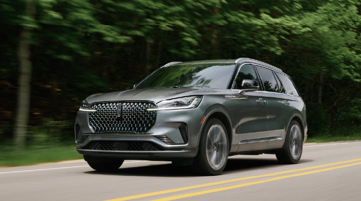 A 2027 Lincoln Aviator® SUV is being driven down a road lined with trees. | Koons Lincoln of Bethesda in Silver Spring MD